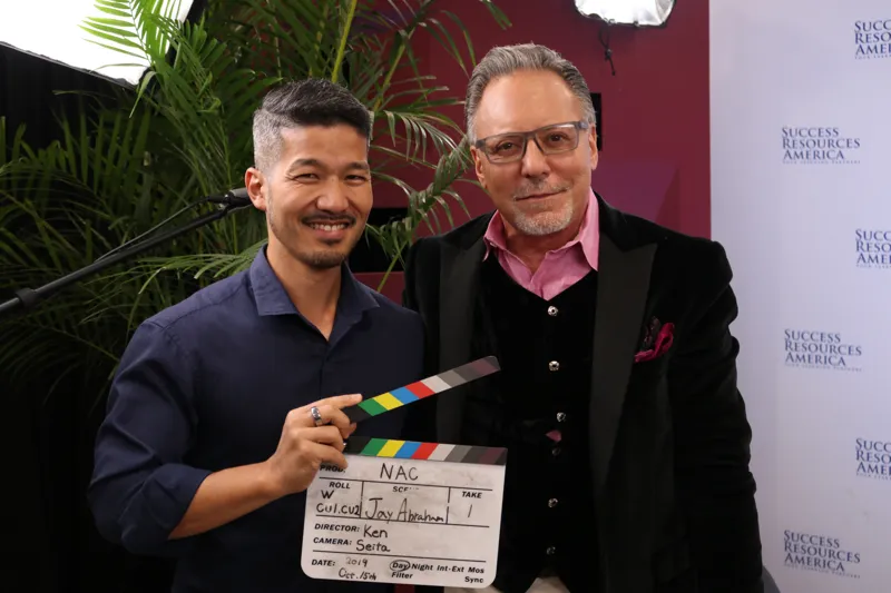 Ken Okazaki with Jay Abraham holding a clapperboard